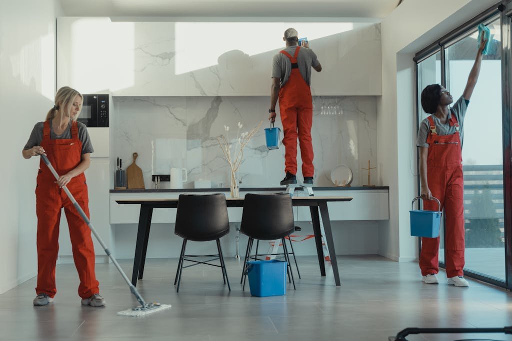 Photo by Tima Miroshnichenko Group of cleaners in red uniforms mopping and wiping glass in a modern dining room.